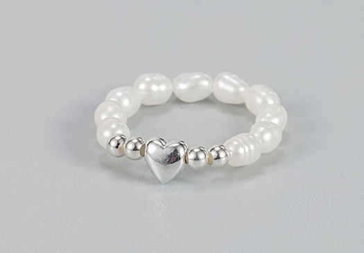 Detalle lateral del anillo de perlas con corazón central en plata sobre fondo gris