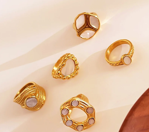 Varios anillos sobre mesa, con el anillo de corazón chapado en oro 18K en el centro, destacando entre ellos