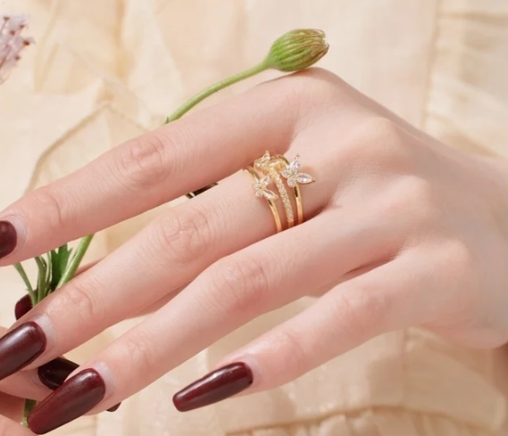 Mano llevando el anillo de mariposas en dorado y plateado/blanco, transmitiendo elegancia y simbolismo.