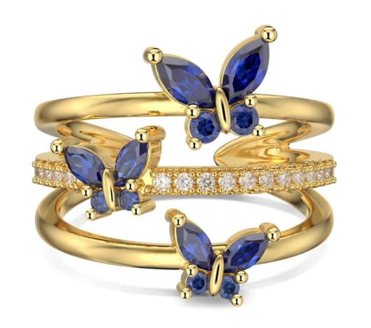 Anillo de mariposas en azul y dorado fotografiado sobre fondo neutro, con detalle de esmalte brillante y estructura en tres aros.