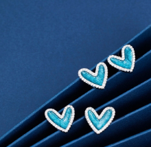 Pendientes de corazón azul con circonitas sobre fondo neutro