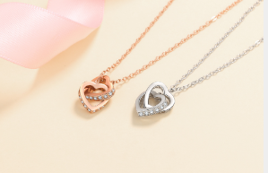 Colgantes tumbados con moissanita en forma de corazón, uno en plata y otro en oro rosa, sobre fondo rosa