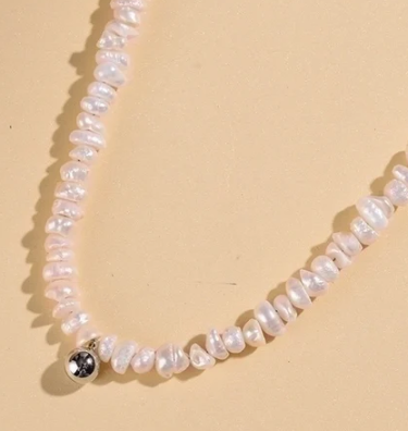 Primer plano del collar de perlas blancas con perla central en plata, fondo beige
