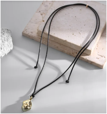 Collar minimalista con colgante lágrima de acero 304 mostrando textura y detalle, colocado sobre piedra blanca, fondo celeste.