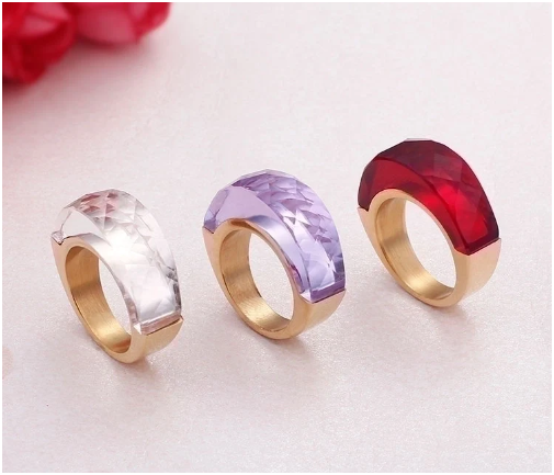 Anillos rojo, cristal y púrpura alineados verticalmente sobre fondo gris claro
