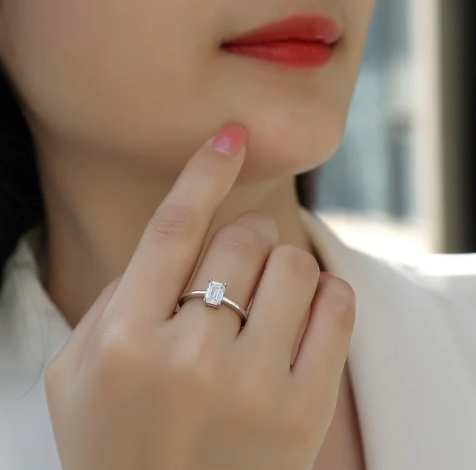 Modelo luciendo anillo rectangular en plata 925 con baño de oro blanco en el dedo corazón, fondo neutro