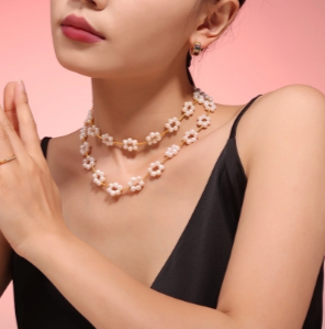 Modelo luciendo dos collares de perlas con margaritas desde el lado izquierdo, estilo en capas con toque romántico