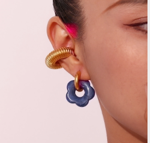 Modelo luciendo pendientes dorados minimalistas en color gris, inspirados en flores bañadas en miel