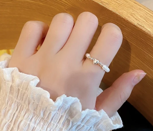Mujer llevando anillo de perlas con corazón central en plata de ley en el dedo índice