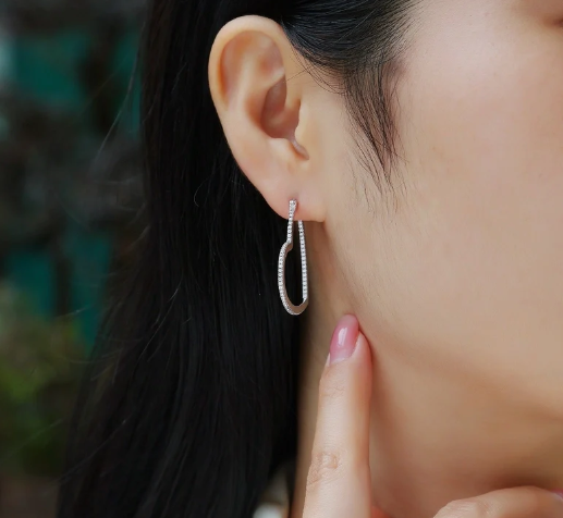 Mujer tocando su oreja y mostrando pendientes grandes de moissanitas en forma de corazón