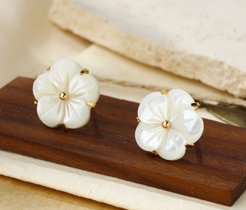 Pendientes de flores de concha natural chapados en oro de 18k exhibidos sobre balda marrón.