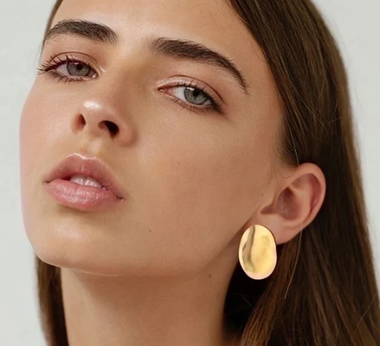 Modelo luciendo los pendientes Grado 888º, realzando el brillo dorado sobre piel bronceada