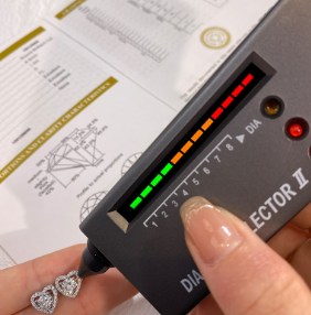 Pendientes de moissanita con tasador mostrando autenticidad en verde y certificado GRA visible al fondo