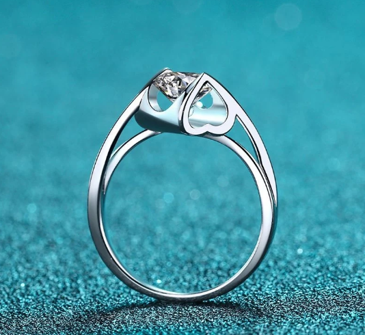 Vista lateral del anillo solitario moissanita con forma de corazón y piedra elevada sobre fondo azul