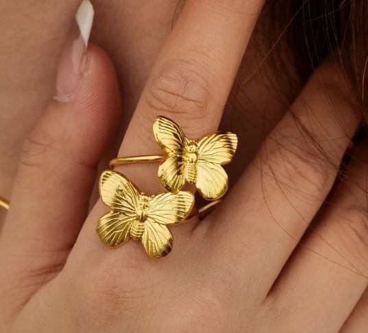 Primer plano del anillo con dos mariposas doradas ajustable en la mano, detalle elegante y simbólico