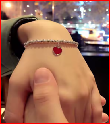 Modelo luciendo pulsera de cuentas chapada en oro con charm rojo en la muñeca.