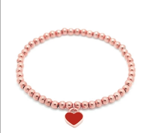 Pulsera de cuentas chapada en oro rosa con charm de corazón rojo sobre fondo blanco.