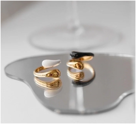 Anillos blanco y negro chapados en oro de 18K reflejados sobre espejo