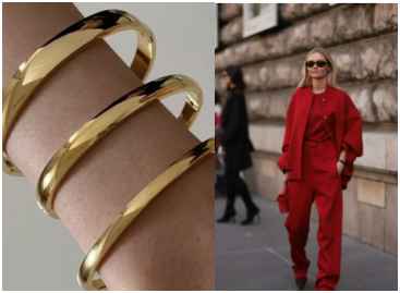 Brazaletes dorados de diferentes medidas combinados con pulseras plateadas junto a modelo con abrigo rojo cereza en la calle, look elegante de otoño-invierno.