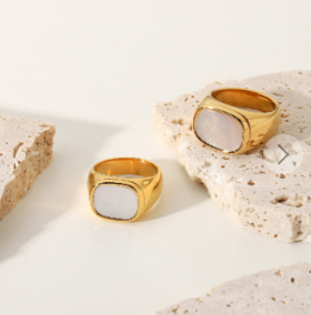 Anillos con concha blanca y baño de oro 18k colocados sobre mármol blanco, composición elegante