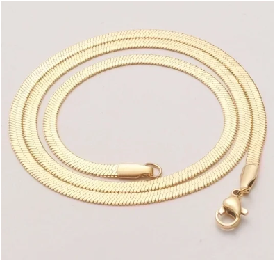 Cadena de hombre en acero de titanio chapado en oro 18K, estilo espiga plana de 5 mm, enrollada sobre fondo beige. El detalle del cierre de mosquetón resalta la calidad y durabilidad de la pieza. Colección Hellochic@s-MEN.