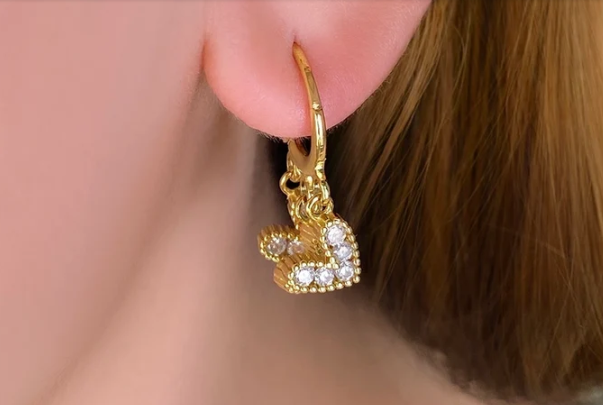 Detalle de los pendientes de aro con charms de corazón en movimiento, captando destellos de luz en fondo neutro