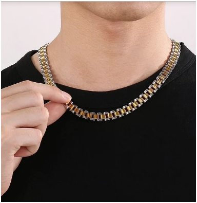 Collar de hombre en acero de titanio chapado en oro y plata, modelo con camiseta negra sujetando el collar con dos dedos. Estilo hip-hop y cierre de mosquetón. Colección Hellochic@s-MEN.