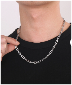 Modelo masculino con camiseta negra sujetando con dos dedos un collar de hombre en acero de titanio chapado en plata de 50 cm. La imagen destaca la longitud y textura de la cadena, mostrando estilo urbano y moderno. Colección Hellochic@s-MEN.