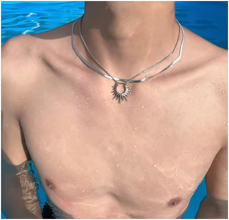 Modelo masculino junto a la piscina llevando collar doble capa en acero de titanio chapado en oro 18K. El brillo de las cadenas contrasta con la luz del agua, evocando frescura, estilo y actitud veraniega. Joyería masculina urbana de la colección Hellochic@s-MEN Otoño-Invierno 2025/26
