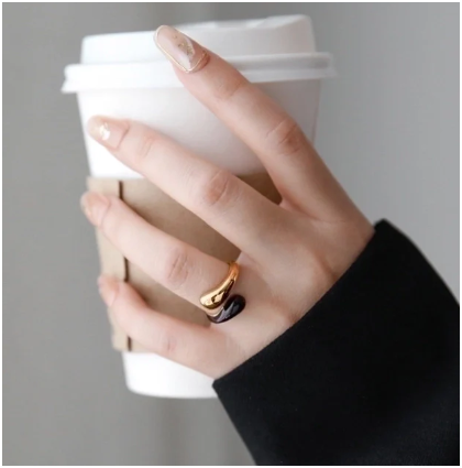 Modelo con anillo negro chapado en oro de 18K mientras sostiene una taza de café
