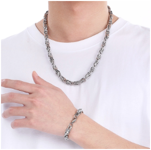 Modelo masculino con camiseta blanca mostrando pulsera de acero inoxidable 305 en muñeca, posando con la otra mano tocando la pulsera.