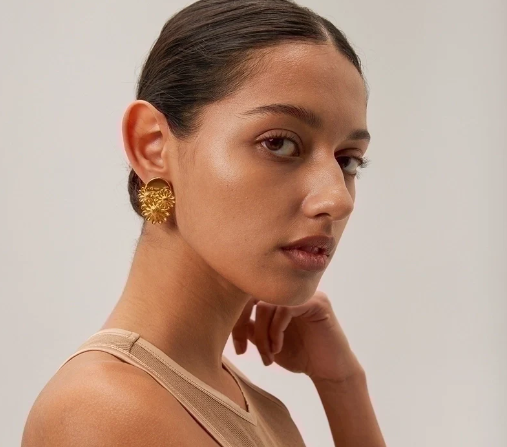 Modelo luciendo pendientes flor chapados en oro 18K, diseño minimalista y elegante para ocasiones especiales