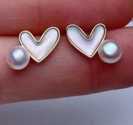 Pendientes de corazón con perla natural mostrados entre los dedos para detalle de tamaño