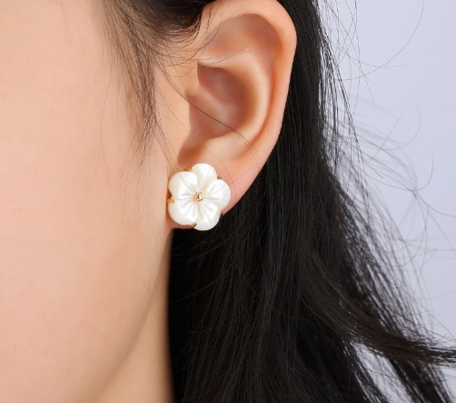 Pendientes florales con concha natural, chapados en oro de 18 quilates, lucidos por modelo.