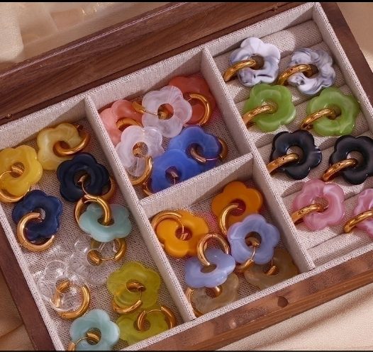 Colección de pendientes dorados minimalistas en varios colores sobre joyero blanco