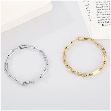 Pulseras de hombre dorada y plateada chapadas en oro 18K y plata con cierre de mosquetón sobre fondo gris junto a un libro
