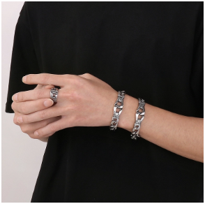 Modelo con camiseta negra mostrando dos pulseras y anillo chapado en oro de 18K, fondo negro, mano acariciando anillo.