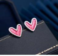 Video mostrando pendientes en forma de corazón con circonitas, en rosa y azul, girando sobre fondo neutro con reflejos de luz que realzan su brillo y detalle